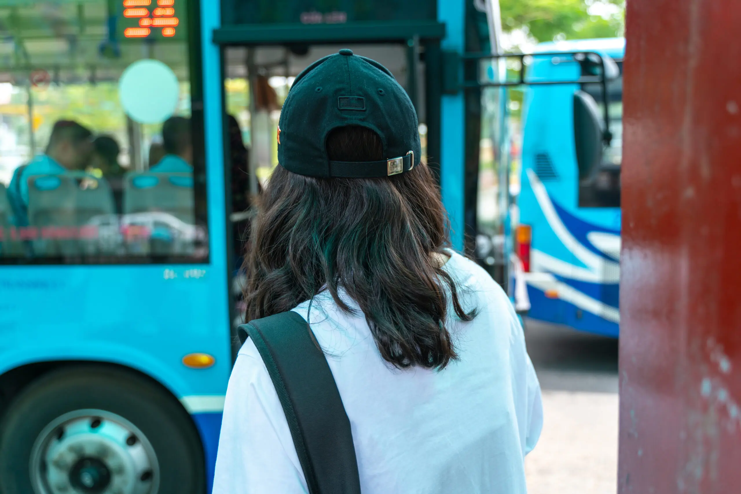A close up view of a woman standing in front of a bus, facing away from the camera.