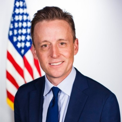Sean Cairncross smiles at the camera in front of an American flag