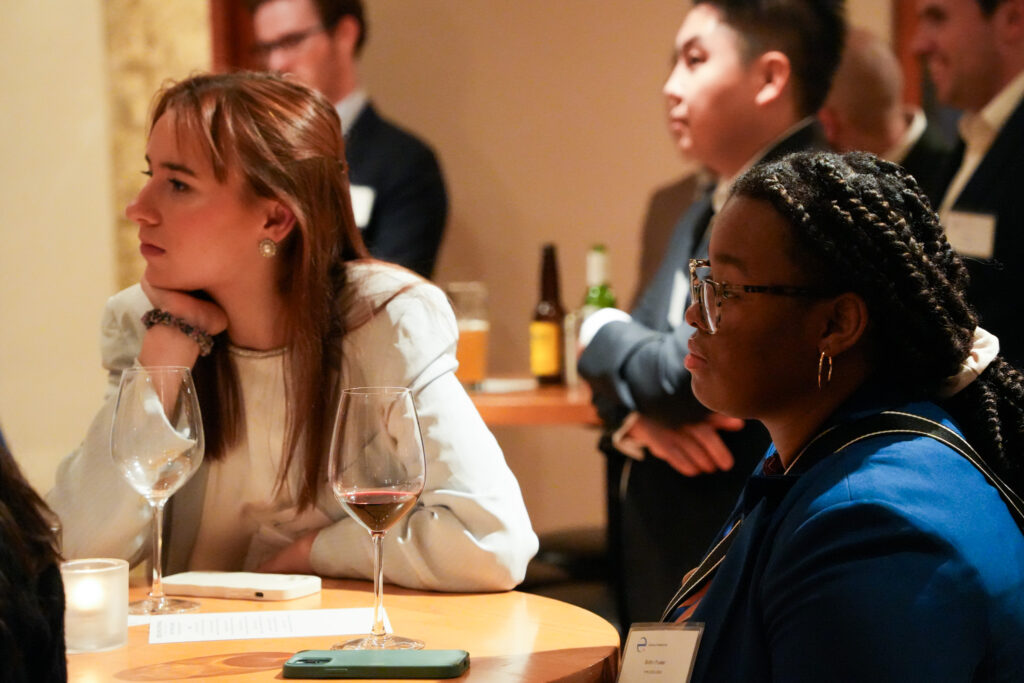 YPN fellows Brittni Foster and Mimi Reitz sit at a table and look attentively at a speaker, who is out of frame.
