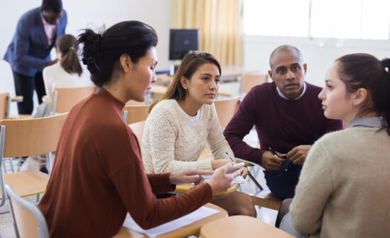 A group of adults sit in a university classroom, deep in discussion.