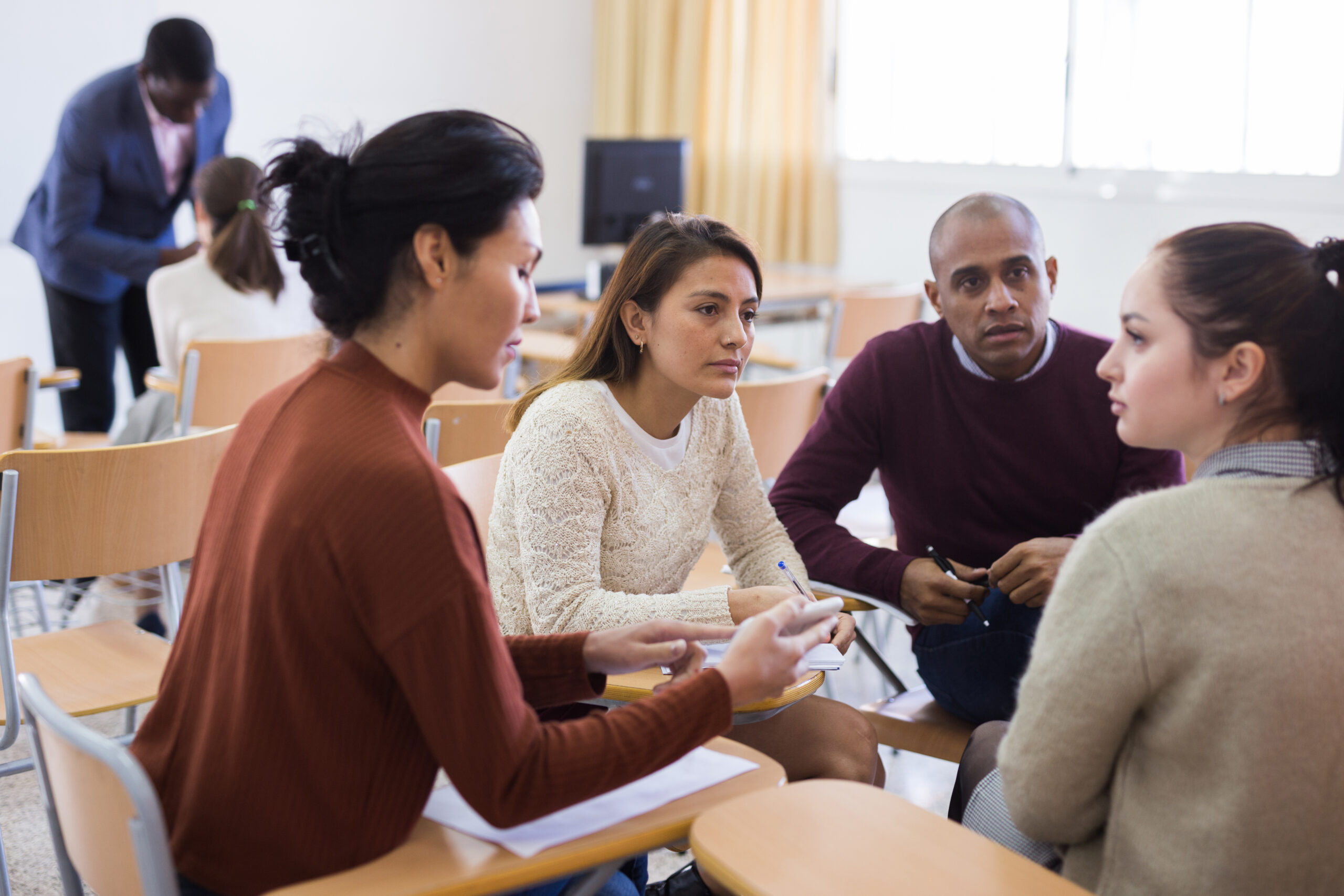 A group of adults sit in a university classroom, deep in discussion.