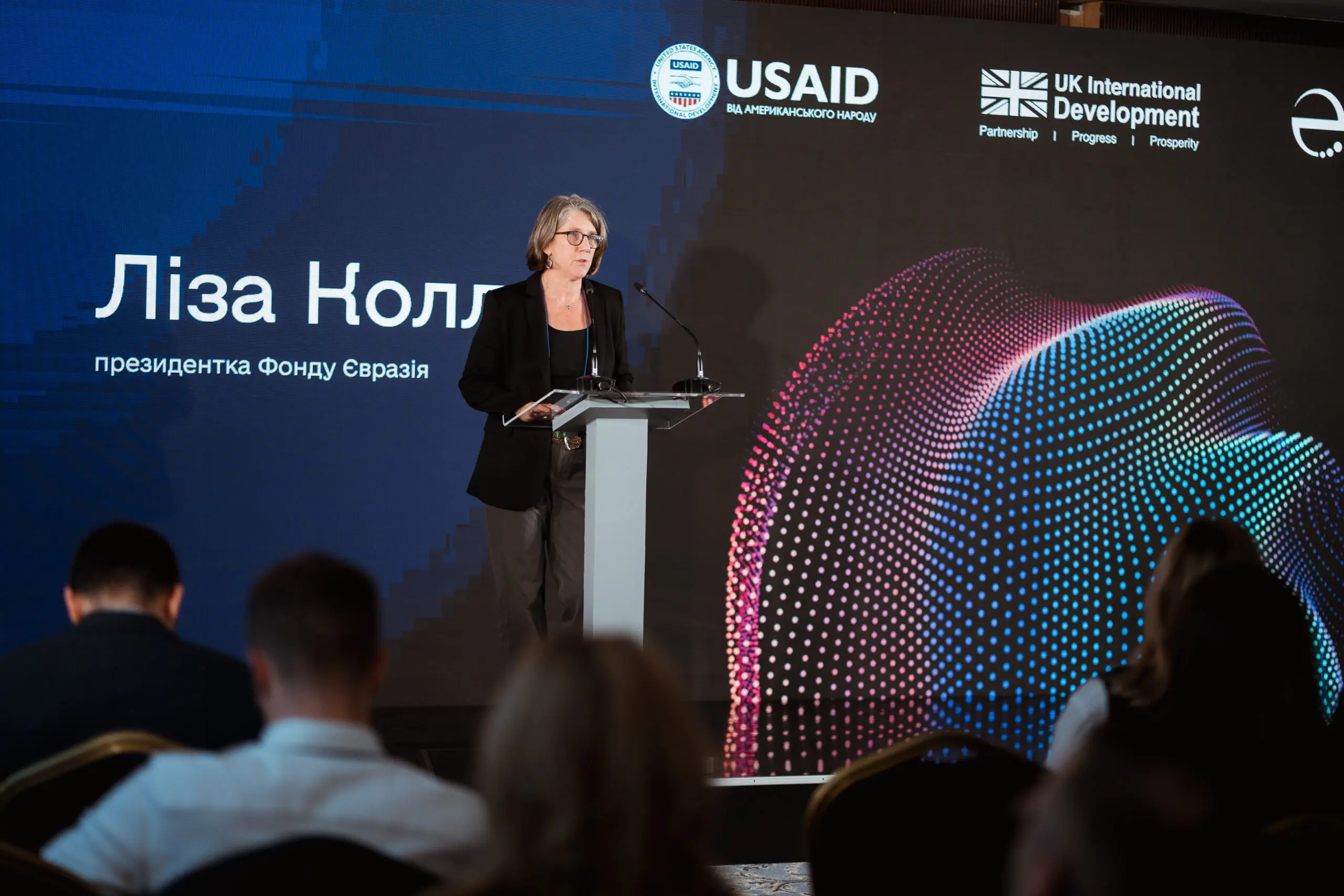 Lisa Coll, EF president, addresses the crowd at the Ukraine Digital Transformation Activity launch event. A screen spanning the stage behind her shows her name in Ukrainian with the USAID and UK Dev logos.