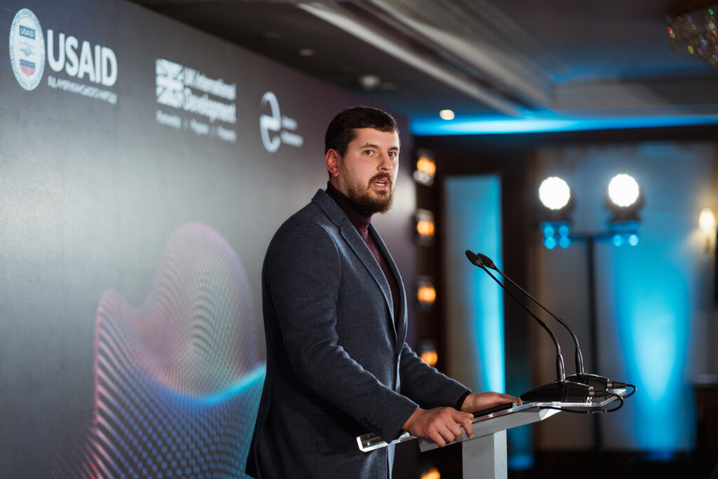 Anatolii grasps the podium and address an audience (out of frame) at the Ukraine Digital Transformation Activity launch event. A backdrop features the UK Dev and Eurasia Foundation logos.