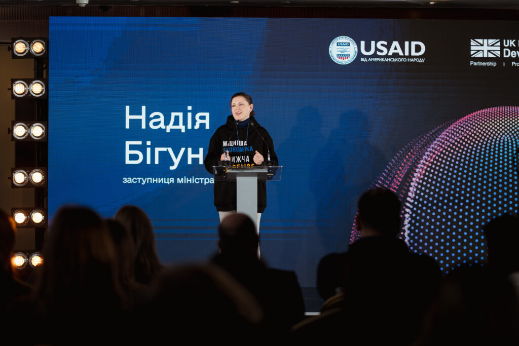 Nadiia speaks to the audience at the Ukraine Digital Transformation Activity launch event. A screen behind her shows her name in Ukrainian and the USAID logo.