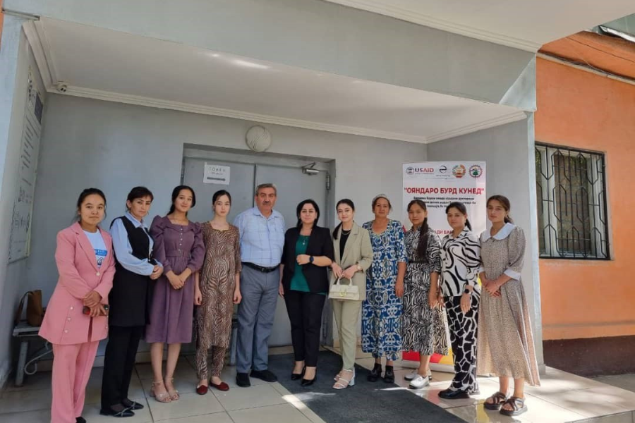 Ten women and one man stand outside of an academic building during a study tour to Tajikistan National University.