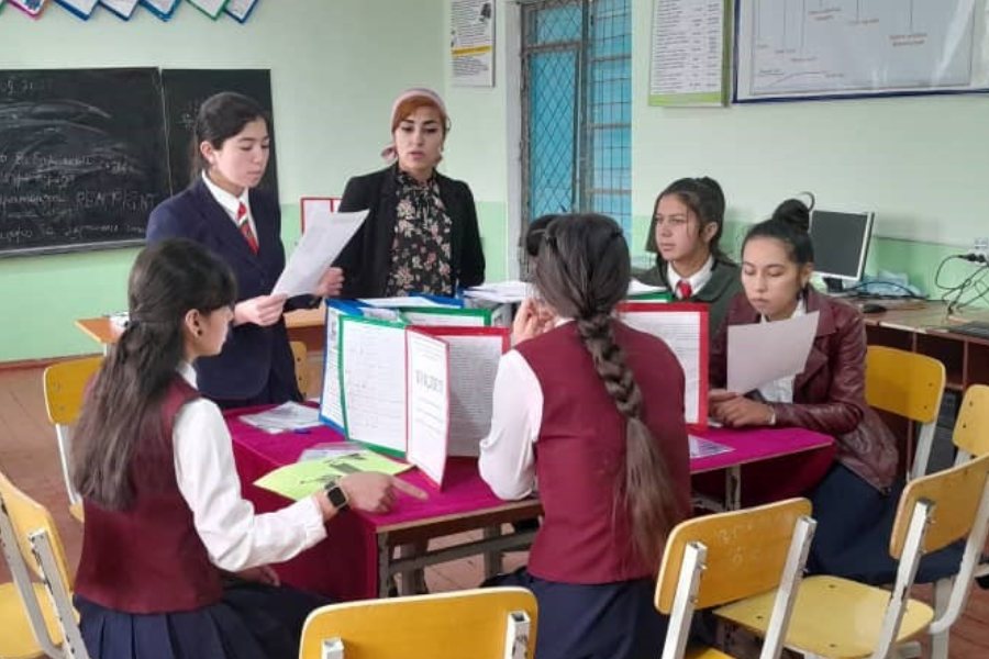 Five schoolgirls and a teacher sit around a cluster of desks, working on a STEM project.
