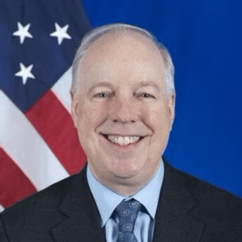A headshot of Kent Logsdon in professional attire in front of the U.S. flag